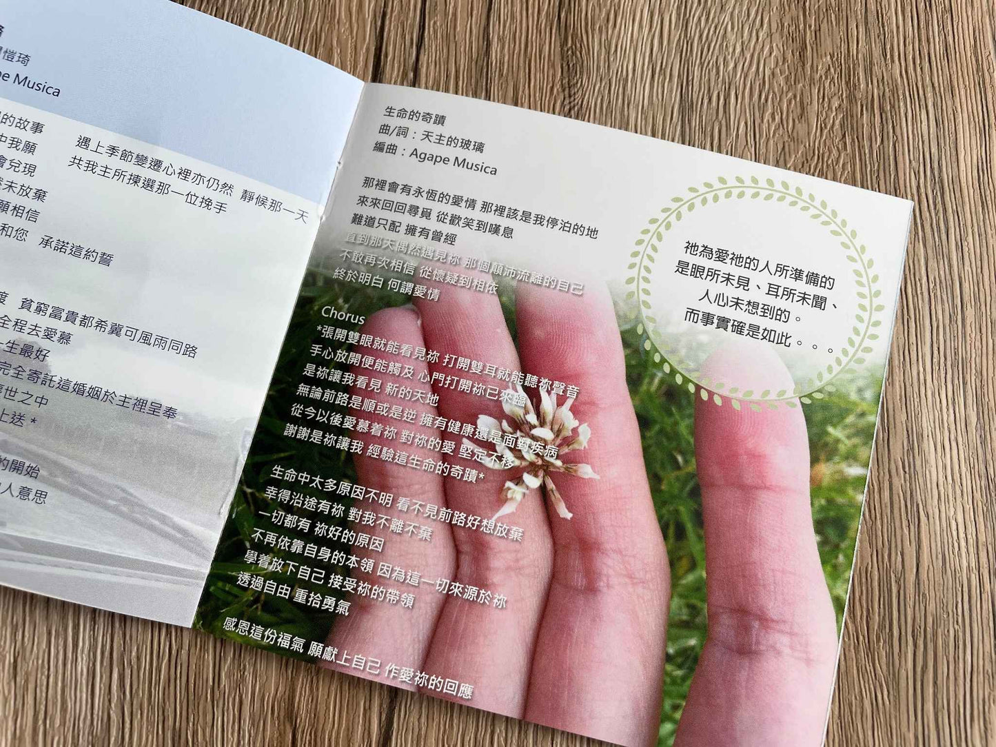 棕色桌面上是已打開的歌詞本,里面是歌曲「生命的奇蹟」的歌詞內容。作曲/作詞是天主的玻璃,編曲是Agape Musica。歌詞頁面右上方印有:祂為愛祂的人所準備的是眼所未見、耳所未聞、人心未想到的。而事實確是如…