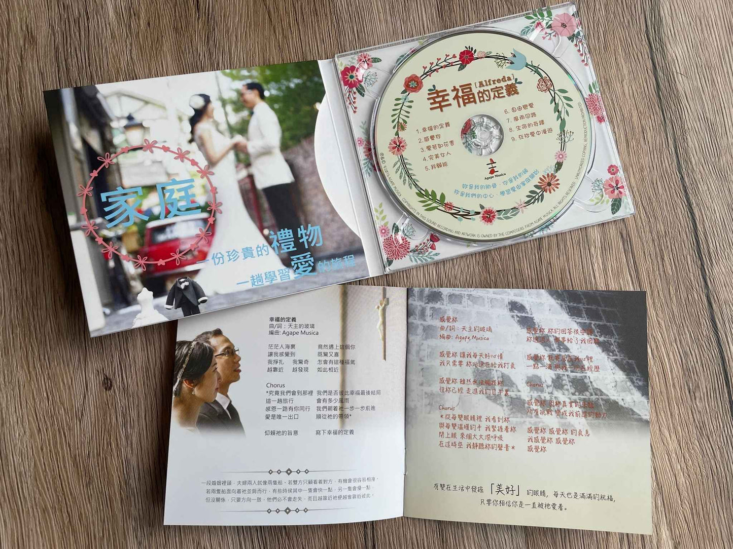 在棕色的桌面上,上面放着的是「幸福的定義」CD打開的包裝,裡面有米黃色的CD;下方是已打開的歌詞本。