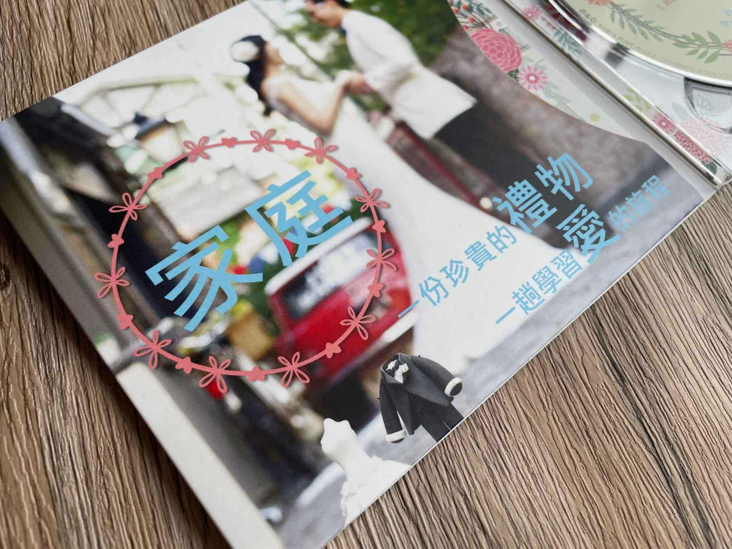 CD包裝內頁背景是一對新婚夫婦,前面印着粉藍色的字:家庭,一份珍貴的禮物,一趟學習愛的旅程。CD包裝底下是棕色的桌面。