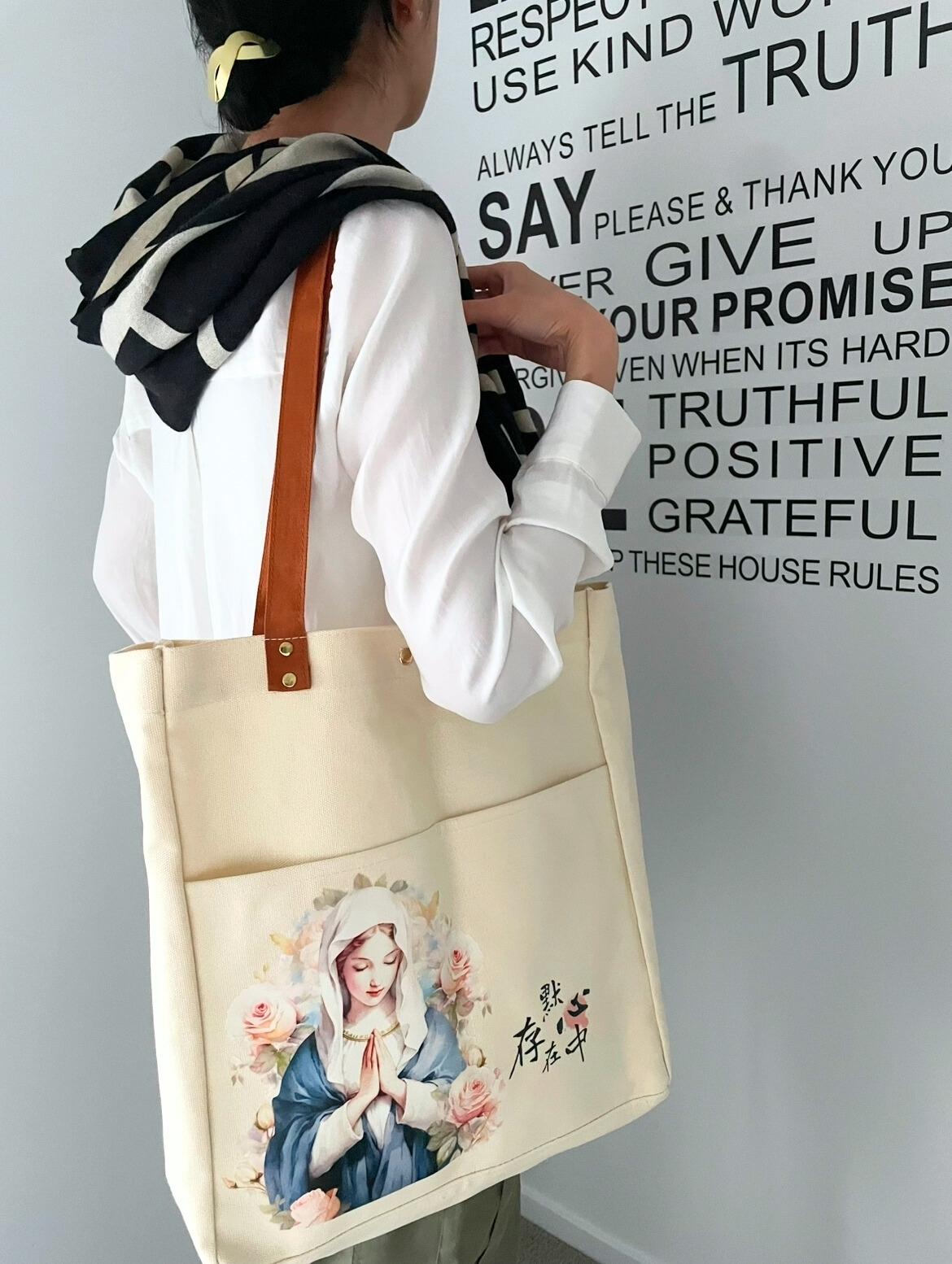 一個身穿白色襯衫肩披藏青色披肩的女生,側身站着望向前面的一面印有黑色英文字的白色牆,右邊肩膀背着一個米色帆布肩背包。包的前面有兩個口袋,左邊印有聖母瑪利亞祈禱的水彩圖案,她的兩旁被玫瑰花包圍,右邊印有「默存在心中」這五個字。兩條肩帶是焦糖色的,與袋口的連接處每邊各有兩顆金色的鉚釘。