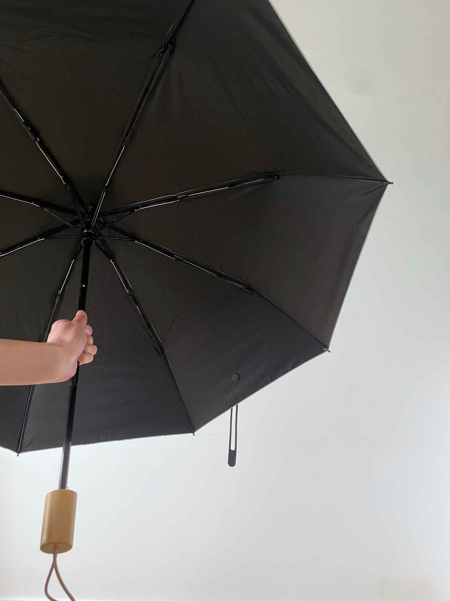 左手邊有一隻手握着一把已打開雨傘的傘杆中間部份。傘內側是黑色的布料和黑色的傘骨及傘杆,手把是木顏色的,並且底部有一條同色的橡筋圈。